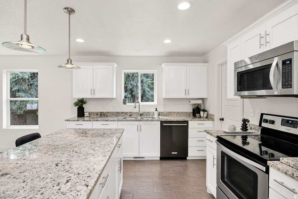 Kitchen featuring a central island with a speckled countertop, white shaker-style cabinetry, stainless steel appliances, recessed lighting, and wood-finish flooring