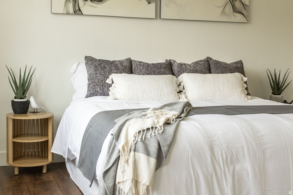 Bedroom featuring wood-finish flooring, light-toned walls, and a slatted round side table