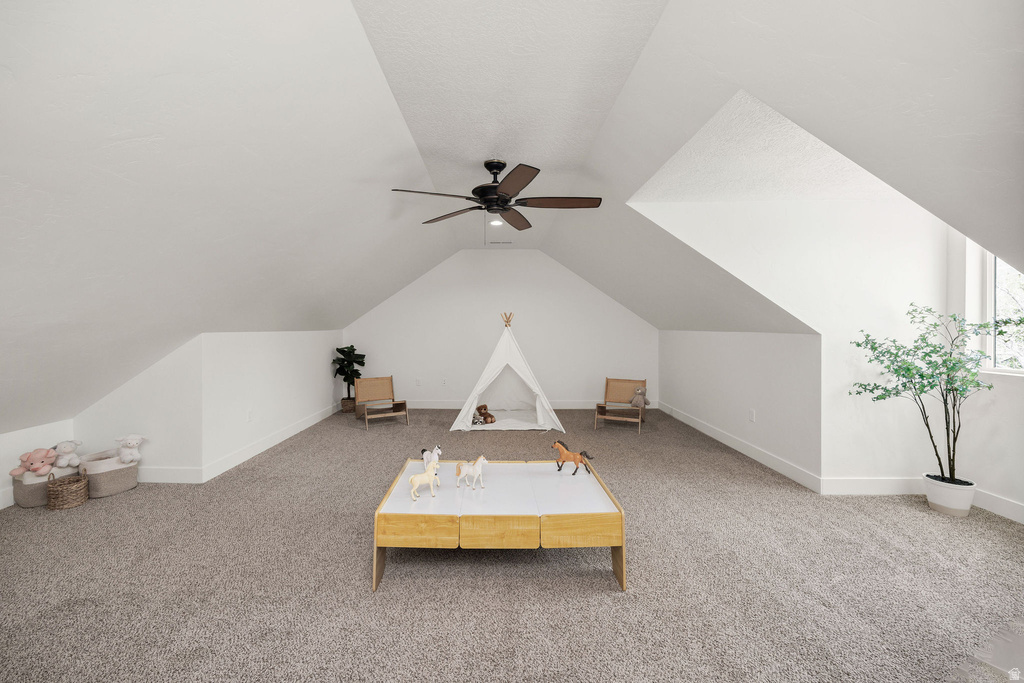 Spacious bonus room featuring vaulted ceilings, plush carpeting, a ceiling fan, and abundant natural light from the window
