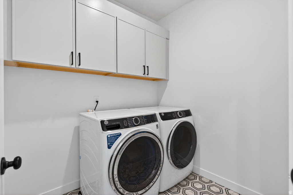 Laundry area featuring white cabinetry with black hardware, a wood-finish shelf, and hexagonal floor tiling