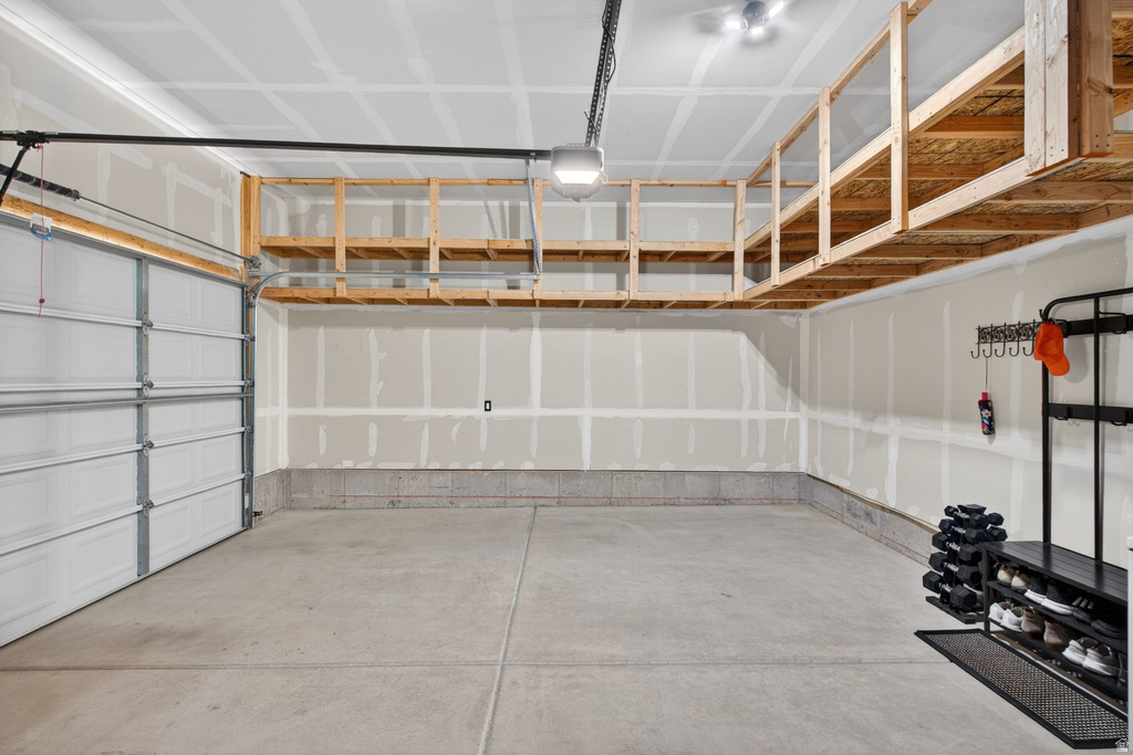 Spacious garage featuring a concrete floor, overhead wood-frame storage shelving, and a white paneled garage door