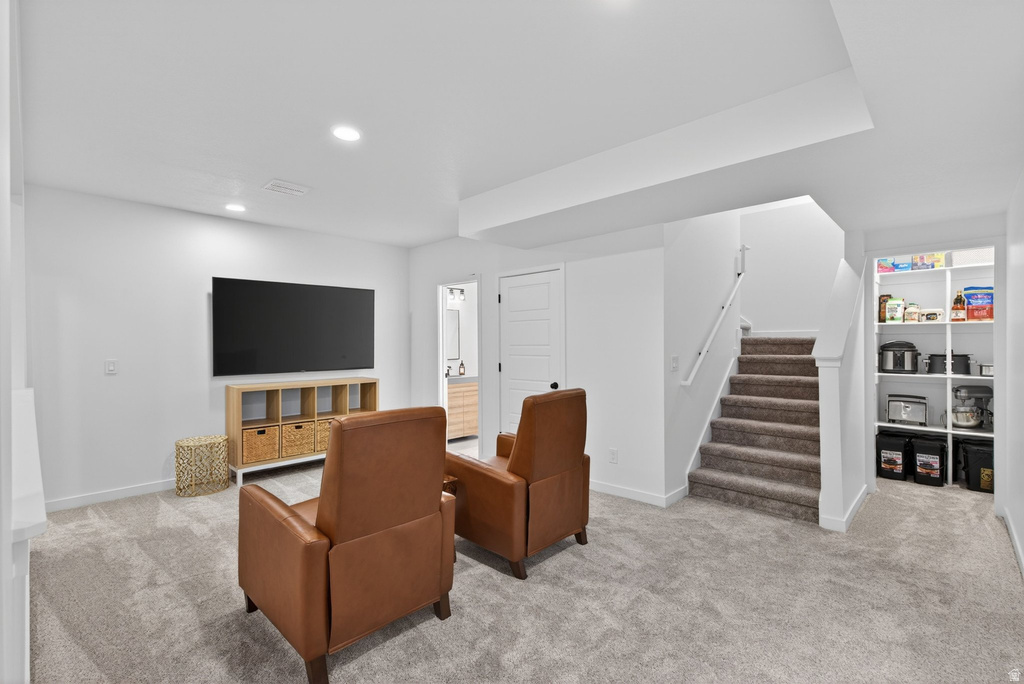 Carpeted recreation room featuring recessed lighting, a built-in shelving unit, and a carpeted staircase with a white handrail