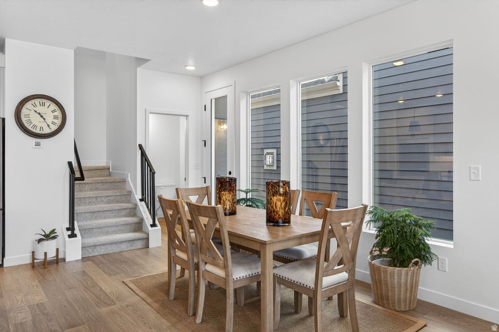 Dining area featuring wood-finish flooring, a wall of multiple windows, recessed lighting, and a staircase with black metal railings
