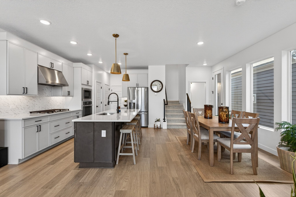 Open-concept living space featuring wood-finish flooring, a contemporary kitchen with light-toned cabinetry, a dark-toned island, and brass pendant lighting