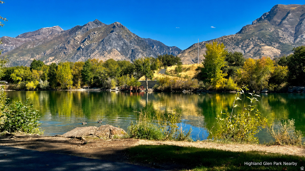 Natural landscape featuring a tranquil body of water, lush green and golden foliage, and a prominent mountain range in the background