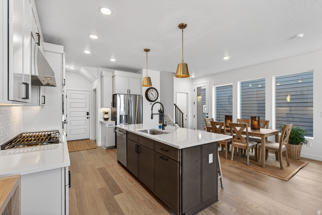 Open-concept kitchen featuring white cabinetry, stainless steel appliances, a central island with a sink, and wood-finish flooring