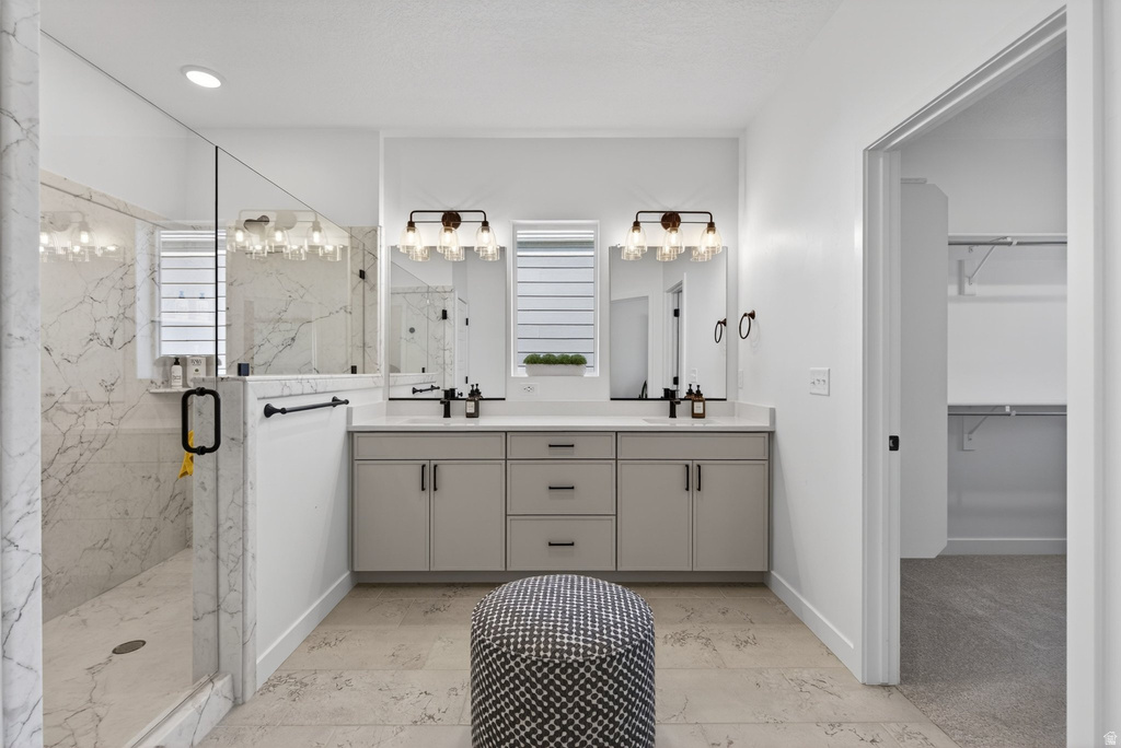 Contemporary bathroom featuring a spacious glass-enclosed shower with marble-look tile, a dual vanity with light gray cabinetry and white countertops, dual framed mirrors, and stylish wall-mounted light fixtures