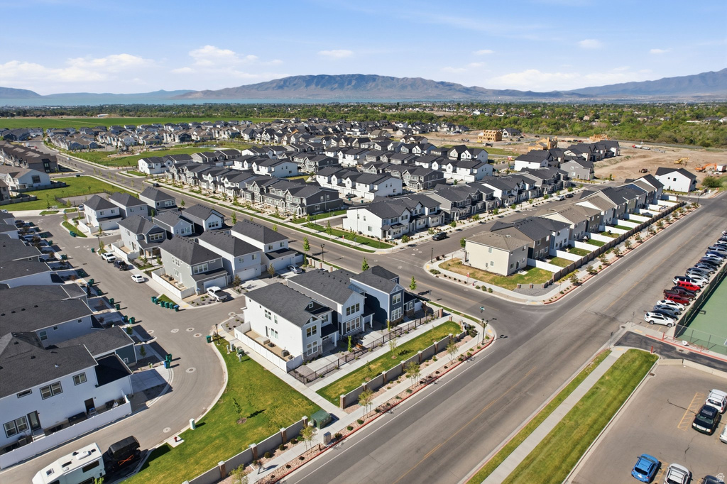 Expansive residential development featuring modern homes with dark roofs, manicured green spaces, paved streets, and mountainous terrain in the distance