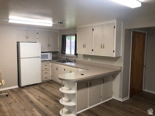 Kitchen with wood-finish flooring, white cabinetry, light-toned countertops, and an integrated breakfast bar with open shelving