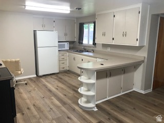 Kitchen featuring wood-finish flooring, white cabinetry, a built-in breakfast bar with open shelving, and a double basin sink