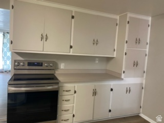 Kitchen featuring extensive light-colored cabinetry, laminate countertops, a stainless steel electric range, and wood-finish flooring
