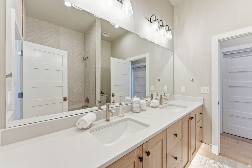 Dual vanity featuring undermount sinks, light wood-finish cabinetry with black hardware, and a substantial wall-mounted mirror