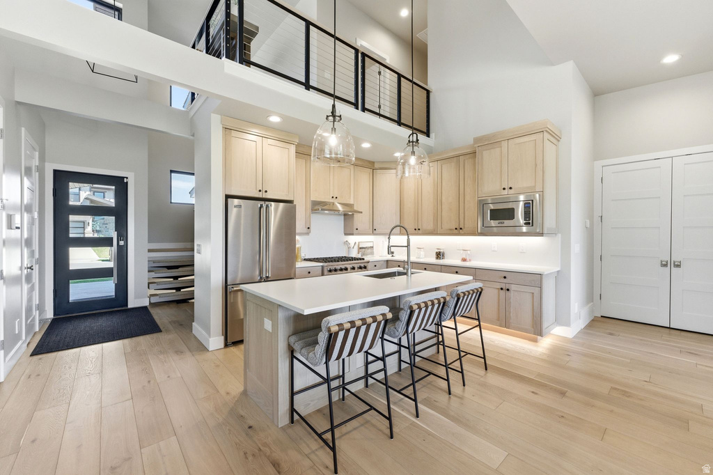 Open-concept kitchen featuring light wood-finish cabinetry, stainless steel appliances, and a central island with a solid surface countertop