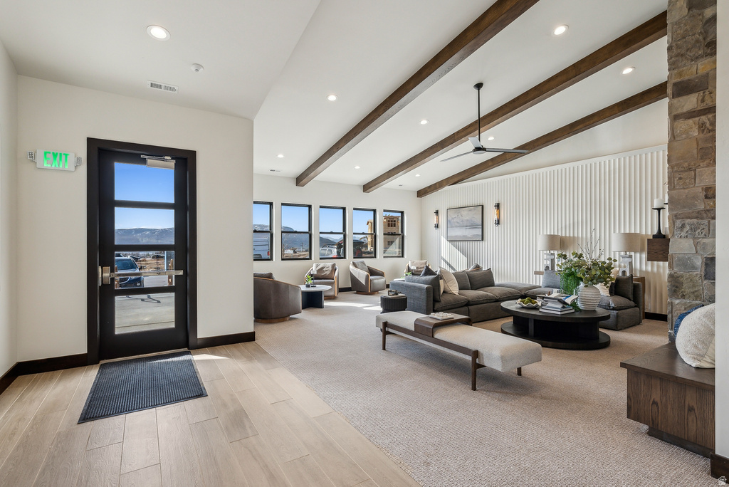 Spacious living area featuring wood-finish flooring, a vaulted ceiling with exposed beams, recessed lighting, and a stone-clad fireplace