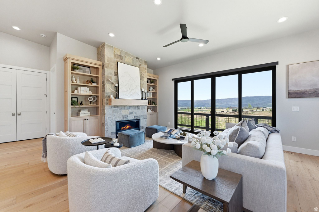 Spacious living area featuring a stone fireplace with a wood mantle, built-in shelving, hardwood flooring, and sliding glass doors opening to a scenic mountain backdrop