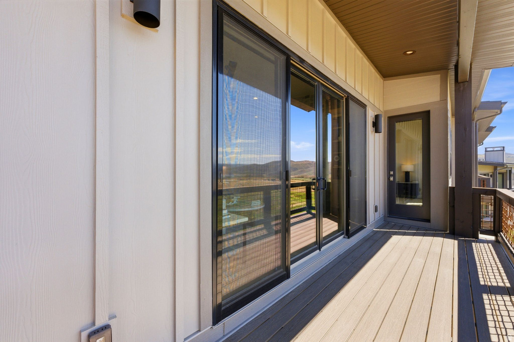 Expansive outdoor deck featuring wood-finish flooring, a sliding glass door system, and a black framed entry door