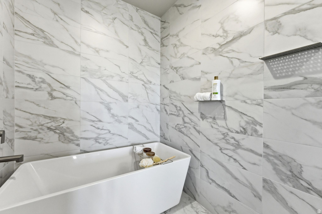 Bathroom featuring a freestanding soaking tub, marble-look wall tile, and a rain shower fixture