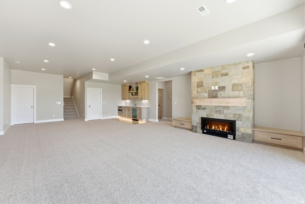 Spacious finished basement featuring a stone-clad fireplace with a natural wood mantel, built-in cabinetry, an integrated wet bar with a wine cooler, and recessed lighting