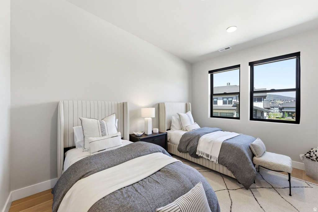 Contemporary room featuring two distinct upholstered wingback beds, recessed lighting, and light wood-finish flooring