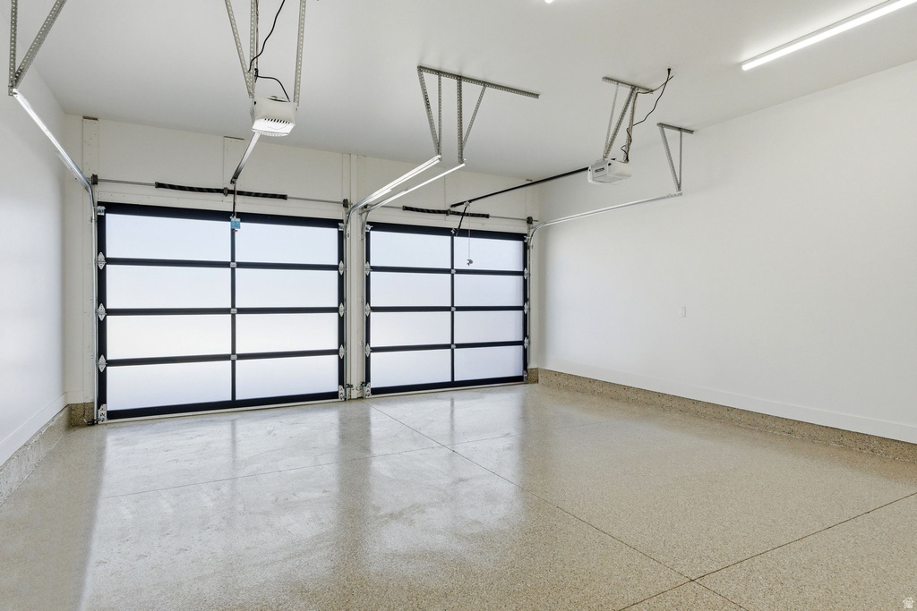 Spacious garage featuring two modern glass panel doors, a durable speckled epoxy floor, bright overhead strip lighting, and automatic garage door openers