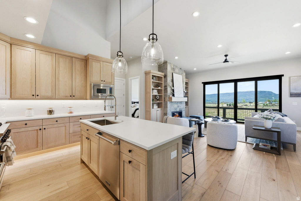 Open concept living space featuring light wood-finish flooring, a kitchen island with integrated sink, stainless steel appliances, and light wood cabinetry
