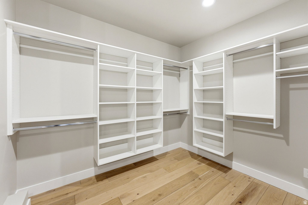 Spacious walk-in closet featuring light wood-finish flooring, white built-in shelving, multiple hanging rods, and recessed ceiling lighting