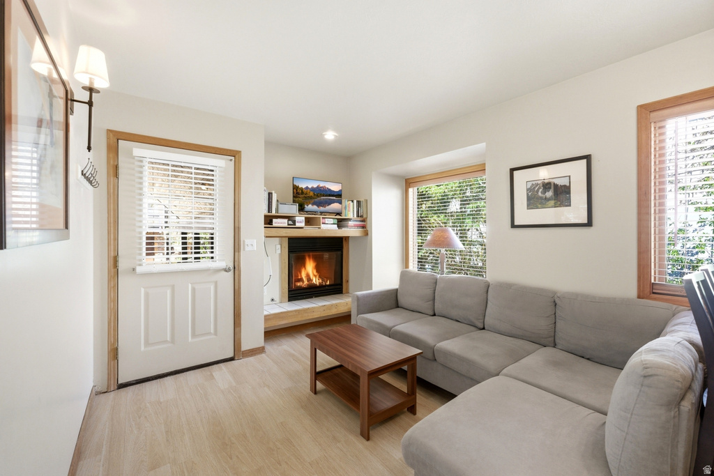 Living area featuring a fireplace with a wood mantle, light wood-finish flooring, and multiple windows with wood trim