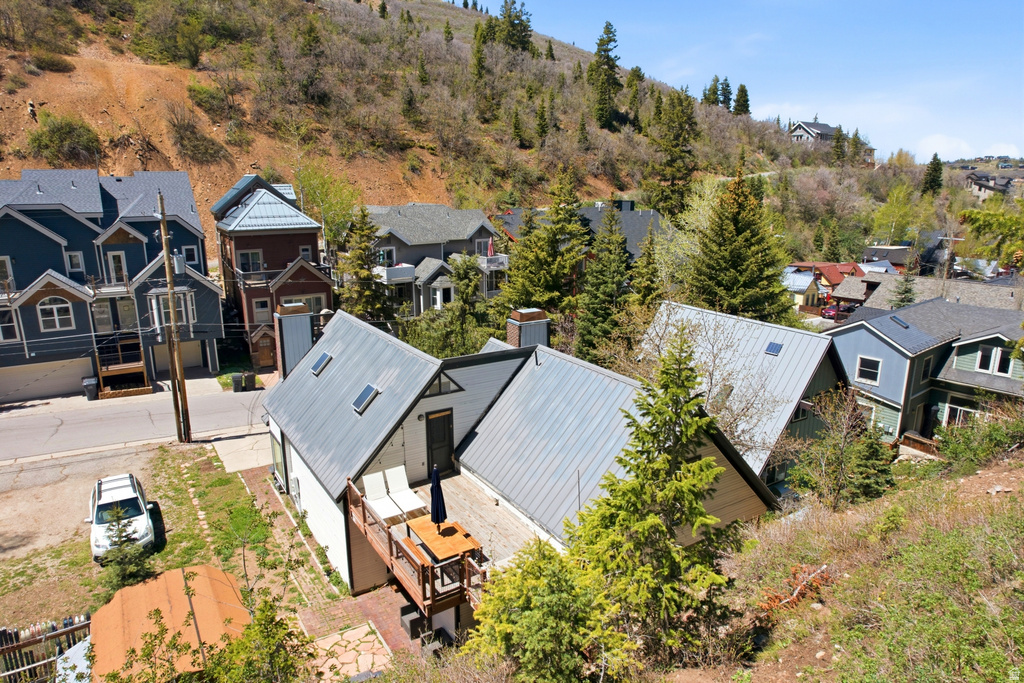 Property featuring a metal roof, an exterior deck, and skylights, set against a backdrop of natural hillside landscaping and mature evergreen trees