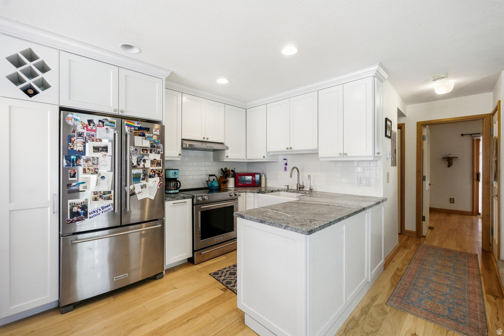 Kitchen featuring white cabinetry, stainless steel appliances, granite countertops, a white subway tile backsplash, and wood-finish flooring