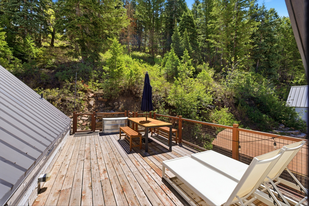 Expansive wood-plank deck featuring a metal roofline, wood and wire railing, and surrounding natural foliage