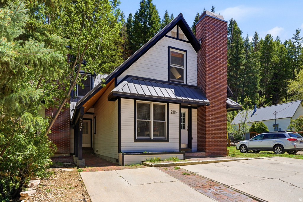 Gabled facade featuring white siding, a metal roof, and a prominent brick chimney