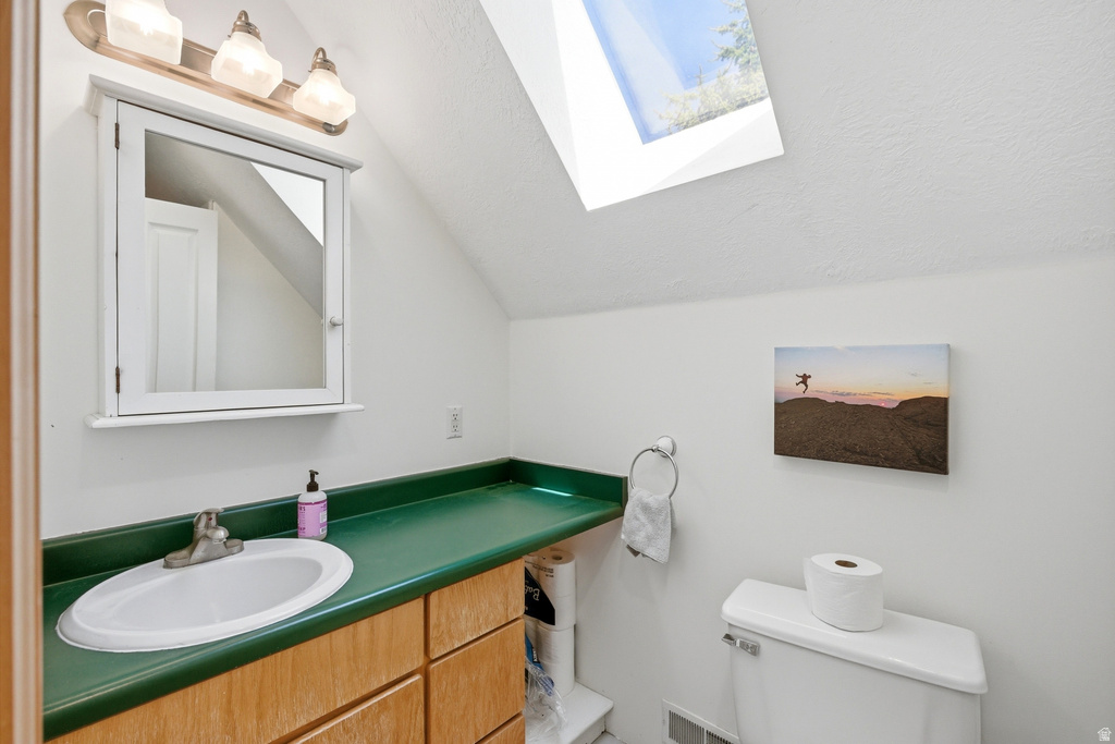 Bathroom featuring a skylight, wood-finish vanity with green countertop, integrated sink, and white medicine cabinet with overhead lighting