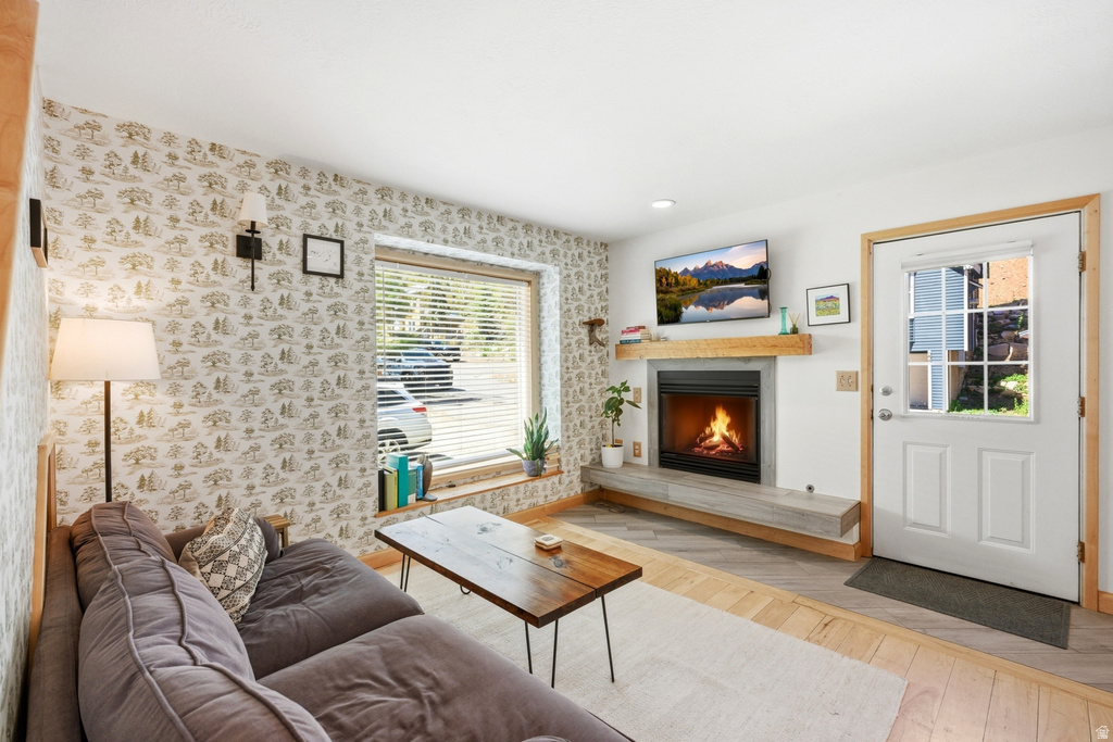 Living area featuring a built-in fireplace with a light wood mantle, a wide window with horizontal blinds, and a white entry door with a multi-pane window insert
