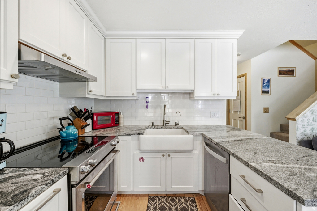 Modern kitchen featuring white shaker cabinetry, patterned stone countertops, stainless steel appliances, a white subway tile backsplash, and a farmhouse-style sink