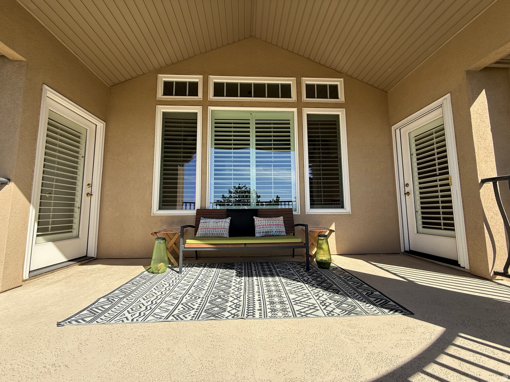 Covered patio featuring an angled wood-finish ceiling, textured exterior walls, multiple windows with plantation shutters, and two glass-paneled doors with internal blinds