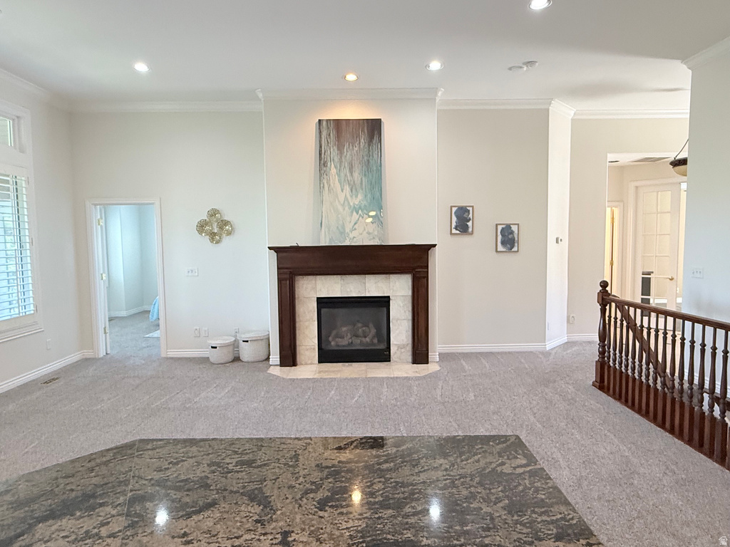 Living area featuring a traditional fireplace with wood mantel and tile surround, recessed lighting, crown molding, and light gray patterned carpet