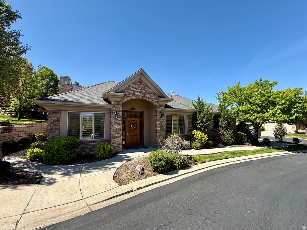 Stone and stucco exterior featuring an arched entryway with a wooden door, surrounded by mature landscaping