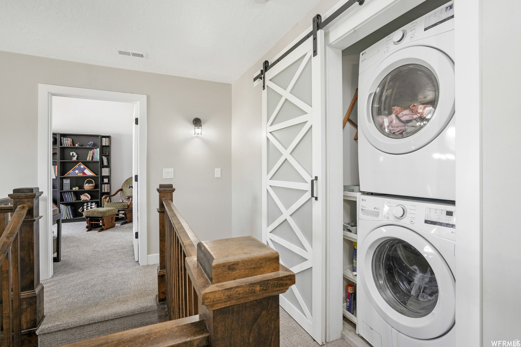 Integrated laundry closet featuring a stacked washer and dryer, complete with a contemporary barn door on a black rail