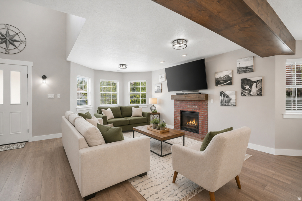 Spacious living area featuring a prominent brick fireplace with a wood mantel, wood-finish flooring, and a vaulted ceiling
