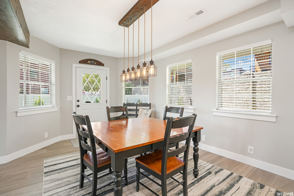 Dining area featuring wood-finish flooring, light gray wall paint, multiple windows with blinds, and a decorative ceiling light fixture with exposed bulbs