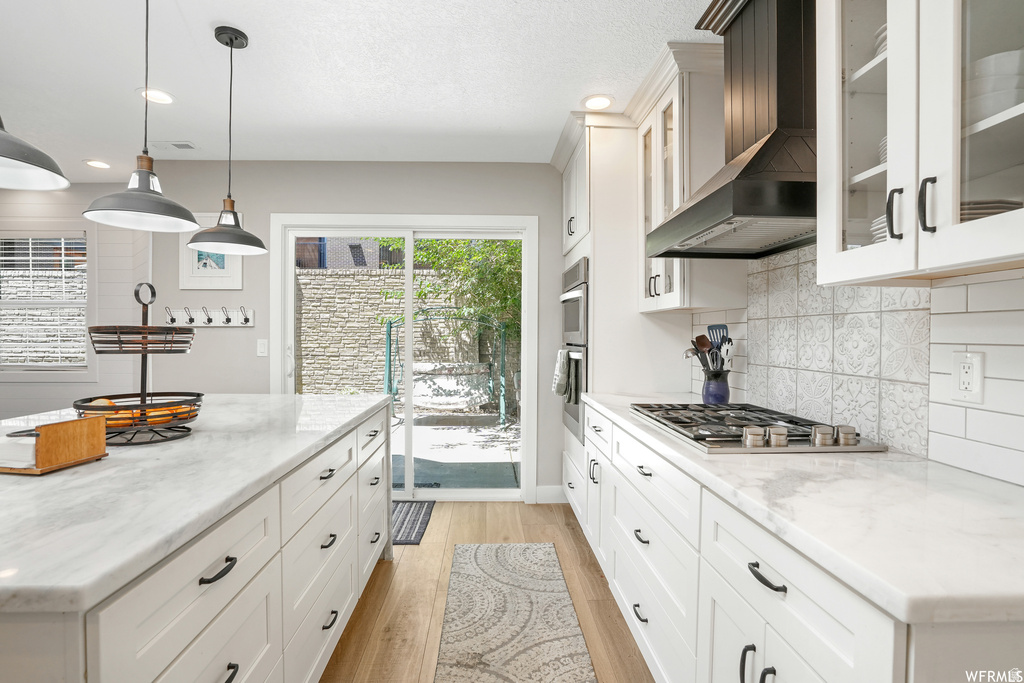 Kitchen featuring white cabinetry, light countertops, wood-finish flooring, and a stainless steel gas range with a dark range hood