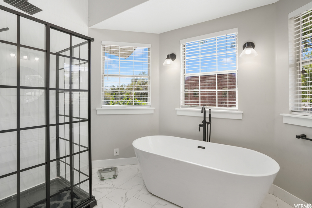 Contemporary bathroom featuring a freestanding soaking tub with a matte black floor-mounted faucet, a grid-patterned glass shower enclosure, and white tile flooring