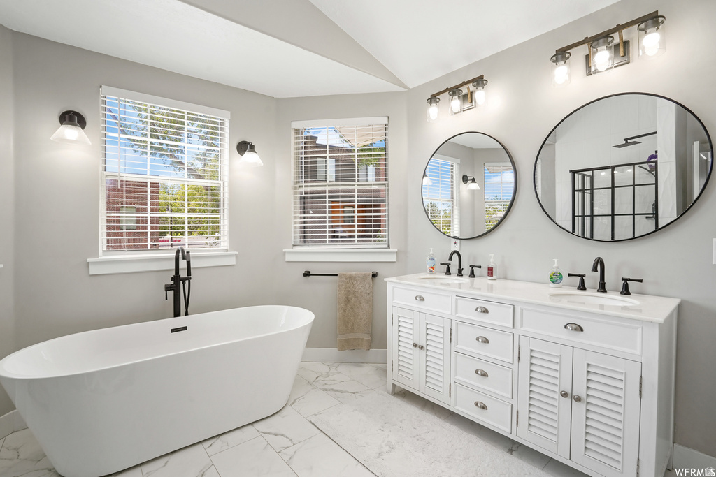 Contemporary bathroom featuring a freestanding soaking tub with a floor-mounted matte black faucet, a dual vanity with white cabinetry and louvered doors, a white countertop, and two large circular mirrors