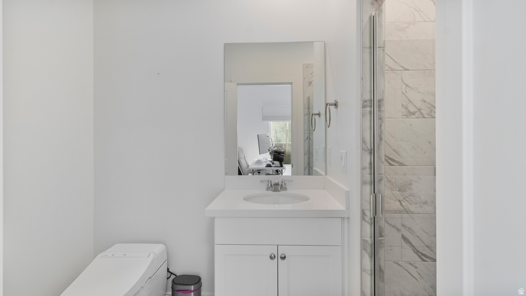 Bathroom featuring a white vanity with an integrated sink and chrome faucet, a rectangular wall-mounted mirror, and a glass-enclosed shower with large format marbled tile