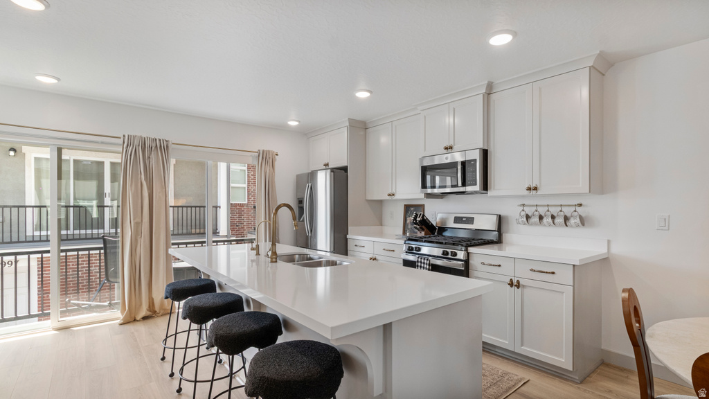 Contemporary kitchen featuring an expansive island with a double sink, white cabinetry, integrated stainless steel appliances, white countertops, and light wood-finish flooring