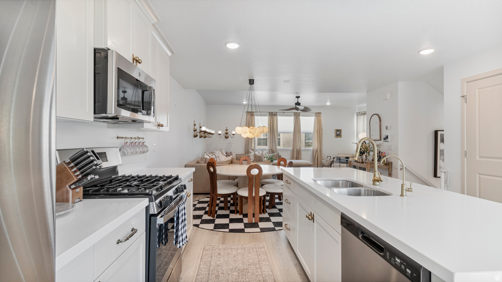 Modern kitchen featuring white cabinetry with gold-tone hardware, stainless steel appliances, and light-tone countertops