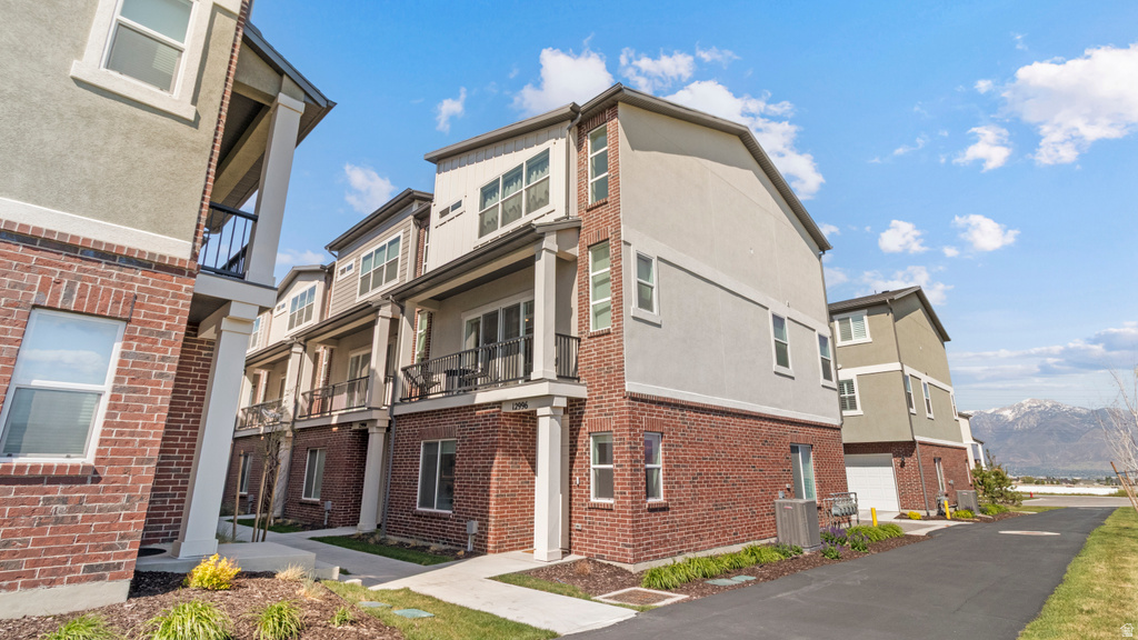 Multi-story townhome with brick and stucco exterior, individual balconies with black railings, and an attached garage