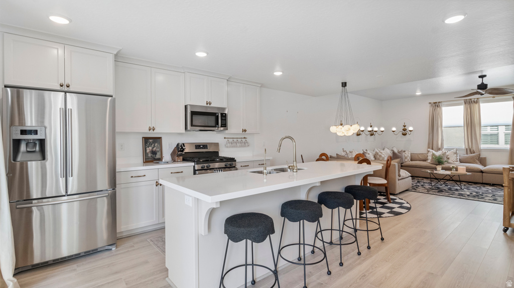 Open-concept living area featuring a kitchen with white cabinetry, stainless steel appliances, a center island with sink, and light wood-finish flooring