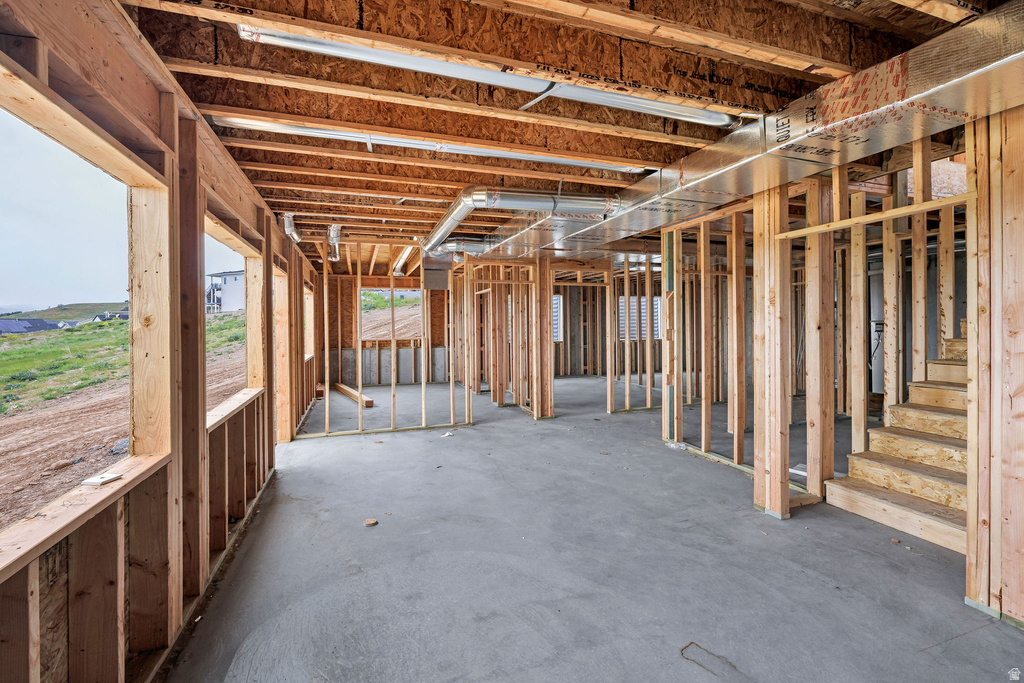 Unfinished basement featuring exposed wood framing, concrete flooring, visible overhead ductwork, and an exposed wood staircase