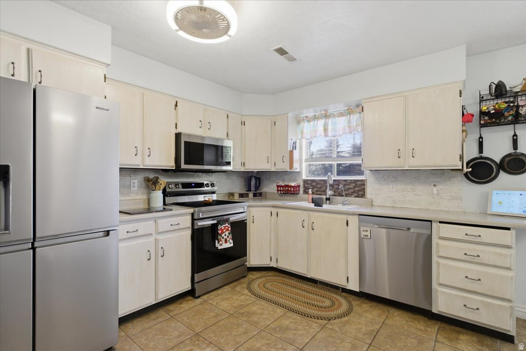 Kitchen featuring light cabinetry, stainless steel appliances, a tile backsplash, and tile flooring